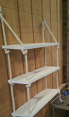 three white shelves with ropes hanging from them on the side of a wooden wall next to a table