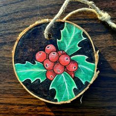 a wooden ornament with holly leaves and berries painted on it