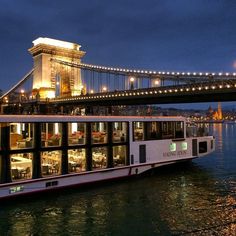 a tour boat on the water under a bridge at night with lights reflecting off it's windows