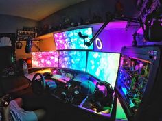 a man is sitting in front of three computer monitors with colorful lights on the screen