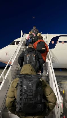 people are boarding an airplane at night on the tarmac with backpacks attached to their backs