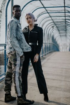 a man and woman standing next to each other in front of a metal fence,