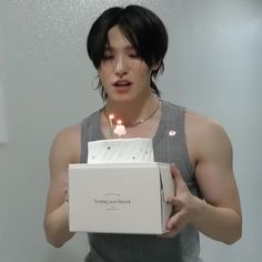 a young man holding a birthday cake with candles in it's box and looking at the camera