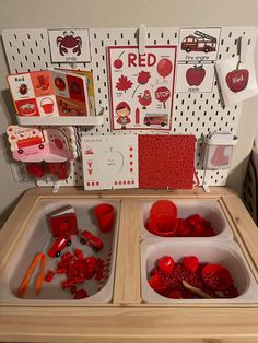 a wooden table topped with trays filled with different types of red objects and cards