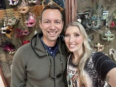 a man and woman standing next to each other in front of masks on the wall