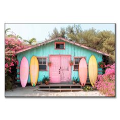 three surfboards leaning against the side of a blue building with pink flowers around it