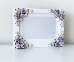 a white frame with pink and blue flowers on it sitting on a table next to a wall