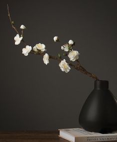 a black vase with white flowers sitting on top of a table next to a book