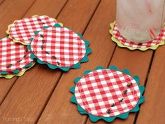 four red and white checkered coasters sitting on a wooden table next to a mason jar