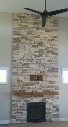 a living room with a ceiling fan and a stone fireplace in the middle of it