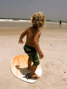 a little boy standing on top of a surfboard in the sand at the beach