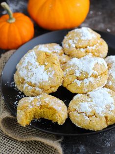 a black plate topped with cookies covered in powdered sugar next to two pumpkins