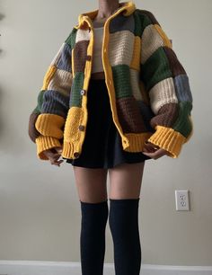 a woman standing in front of a wall wearing knee high socks and a multicolored sweater