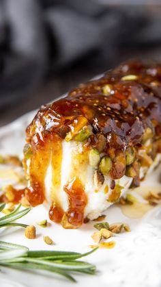 a close up of a piece of food on a plate with sauce and nuts around it