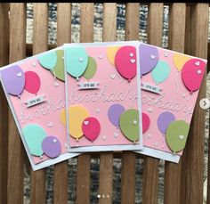 three birthday cards with balloons and confetti on them, sitting on a wooden bench