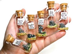 a hand holding six miniature bottles with tiny animals in them, each filled with sand