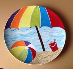 a colorful plate with an umbrella and beach scene painted on the front is hanging on a wall