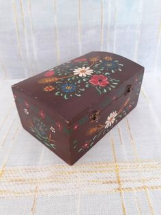 a decorative wooden box sitting on top of a white cloth covered tablecloth with flowers painted on it