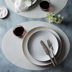 two white plates with silverware on them next to some wine glasses and napkins