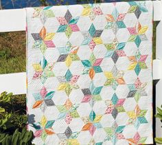 a white fence with a quilt hanging from it's side and flowers in the foreground