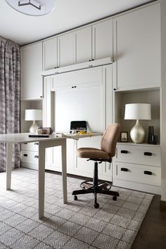 a desk with a chair and lamp in a room that has white cabinets on both sides