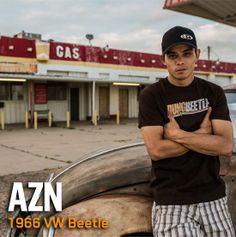 a man standing next to an old car in front of a gas station with his arms crossed