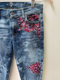 a pair of blue jeans with pink flowers on them hanging from a clothes hook, in front of a white wall