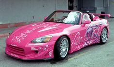 a pink sports car parked in front of a building with graffiti painted on the side