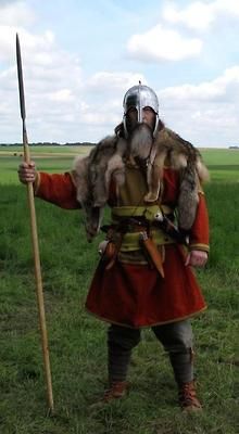 a man dressed in medieval clothing holding a spear and wearing a fur collared coat