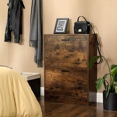 a bedroom with a wooden dresser next to a potted plant and coat rack on the wall