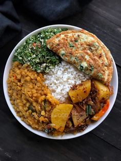 a white bowl filled with rice and vegetables next to a piece of bread on top of a wooden table