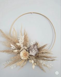 an arrangement of dried flowers and plants in a hoop on the wall with white background