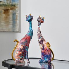 two colorful cats sitting on top of a table next to a bottle and reed diffuser