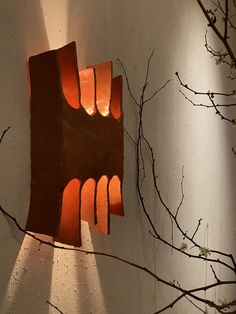 a sculpture is shown on the wall next to a tree branch with its light shining through it