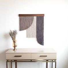 a white table topped with a vase filled with flowers next to a wall hanging on the wall