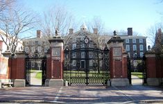 an iron gate in front of a large brick building with a clock on the top