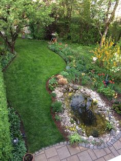 a garden with lots of green grass and flowers on the side of it, along with a small pond