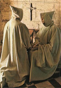 two people dressed in robes sitting next to each other on a bench with a cross behind them