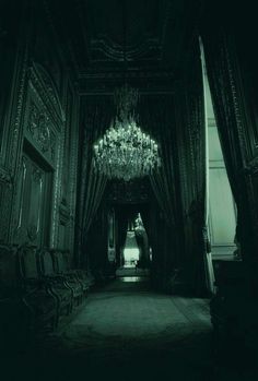 an empty hallway with chandelier and chairs