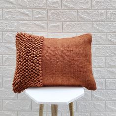 a brown pillow sitting on top of a white table next to a brick wall and wooden stool