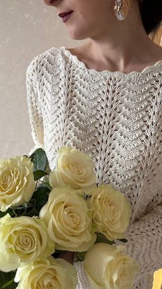 a woman holding a bouquet of yellow roses in her hands and wearing a white sweater