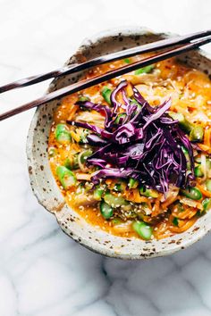 a bowl filled with noodles and vegetables next to chopsticks on a marble surface