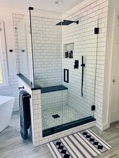 a white tiled bathroom with black and white rugs on the floor, shower stall door and towel rack