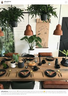 a wooden table topped with black plates covered in food next to potted plants and hanging lights