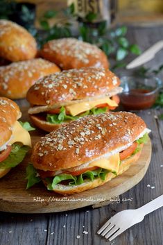 sandwiches with cheese and lettuce are on a wooden plate next to silverware