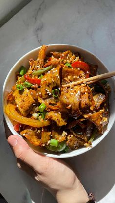 a person holding a bowl of food with chopsticks