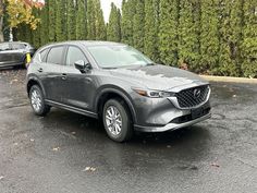 a gray mazda cx - 5 parked in a parking lot next to some trees