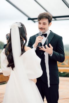 a man in a tuxedo holding a microphone next to a woman in a wedding dress