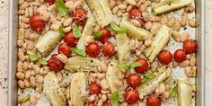 a pan filled with beans, tomatoes and artichokes on top of a table