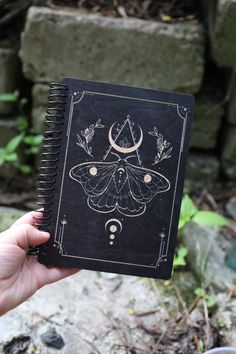 a hand holding up a black book with an image of a moth on the cover